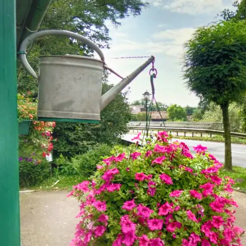 Eine Gießkanne, an der ein Blumenkübel aufgehängt ist, hängt von der Wand